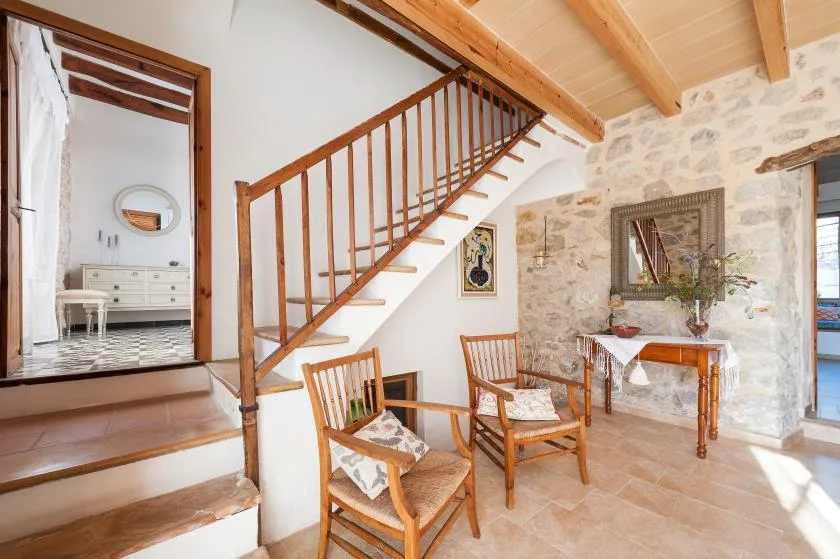 A stone-walled living area with wooden seating and a staircase.