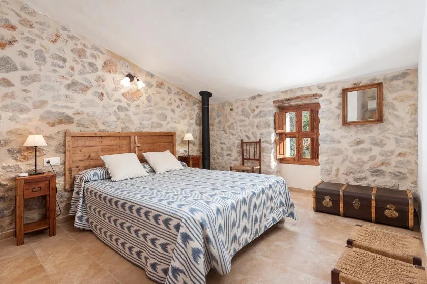 A bedroom with a double bed, stone-patterned walls, and a wooden window.