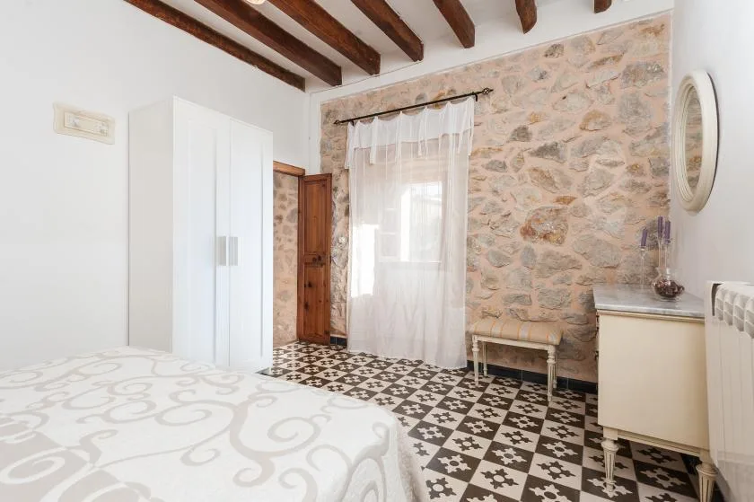 A bedroom with a bed, wardrobe, and a window set in a stone wall.