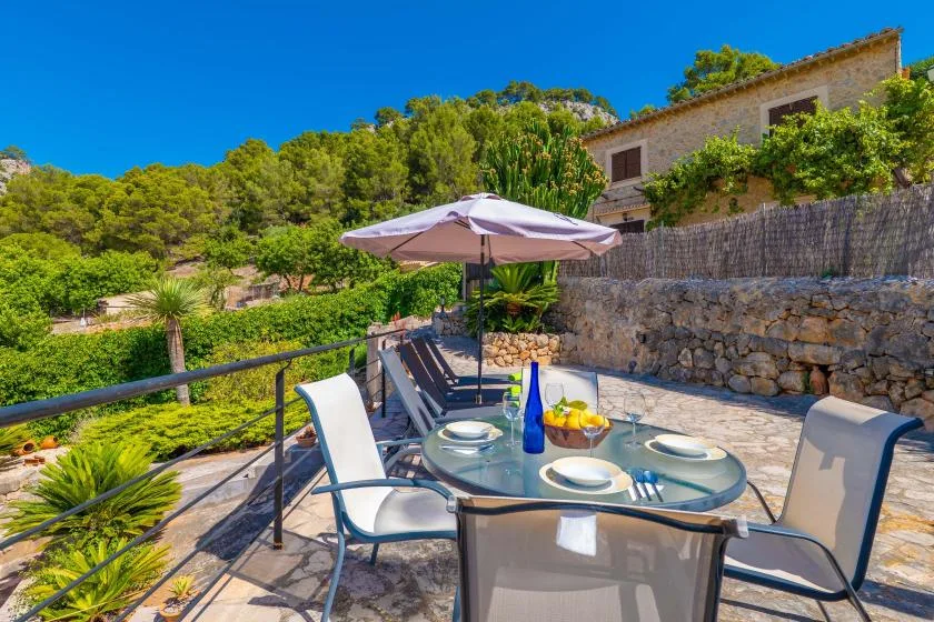 An outdoor dining area with a glass table and umbrella overlooks a green hillside.
