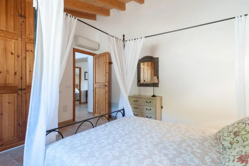 A bedroom with a bed, wooden wardrobes, and white curtains.