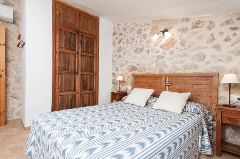 A bedroom with a double bed, wooden headboard, and stone-patterned walls.