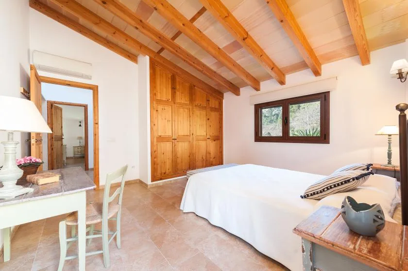 A bedroom with a bed, wooden wardrobes, and exposed ceiling beams.