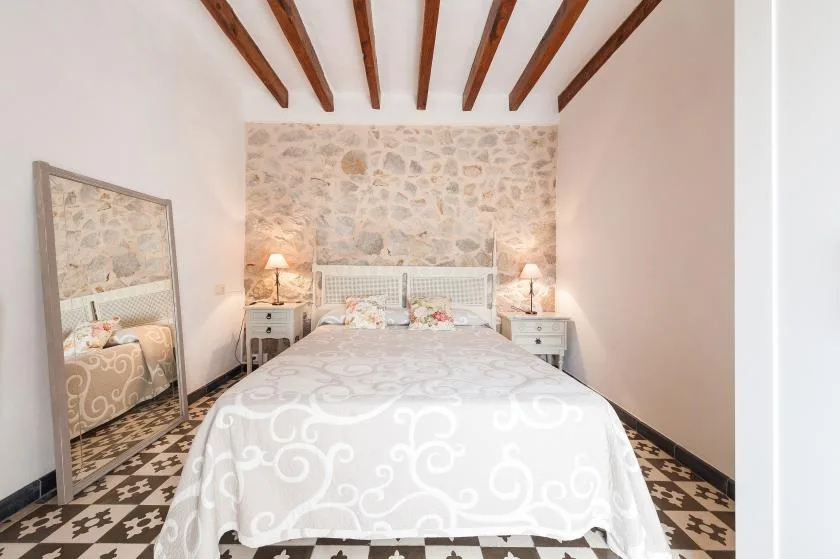 A bedroom with a patterned bedspread, matching bedside tables, and exposed ceiling beams.