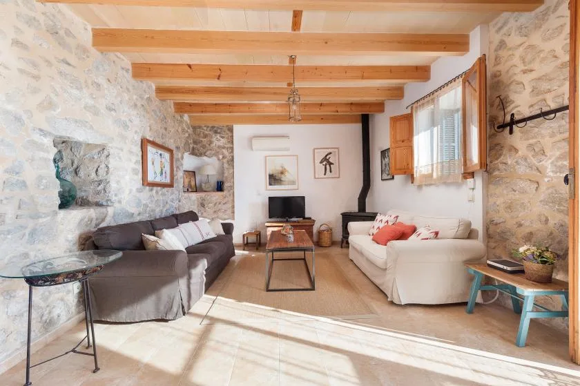 A bright living room has two sofas, exposed wooden beams, and stone walls.