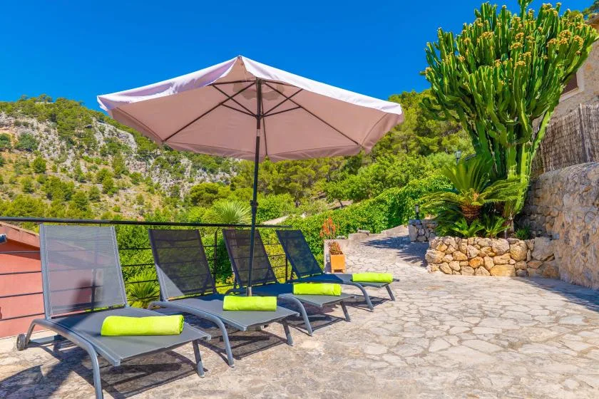 Un patio de piedra soleado tiene asientos reclinables bajo una gran sombrilla rosa.