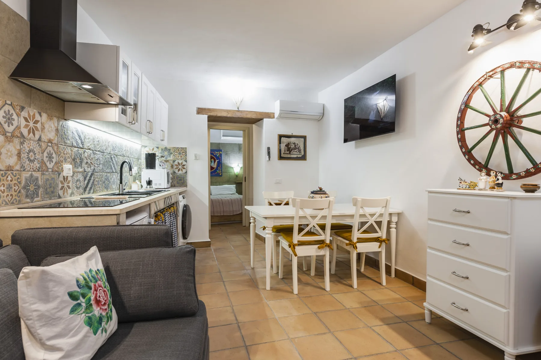 Una cocina compacta y zona de comedor se abren a una sala con un sofá gris.