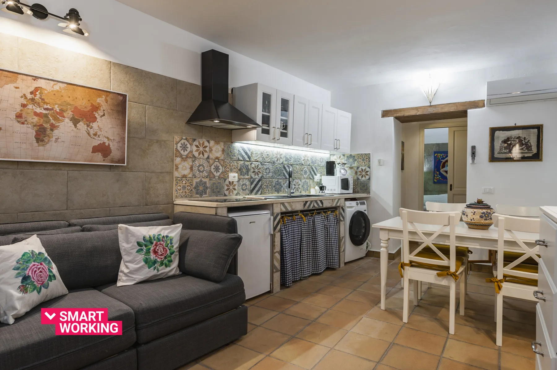 Una sala-comedor diáfana con un sofá oscuro y una cocina con azulejos.