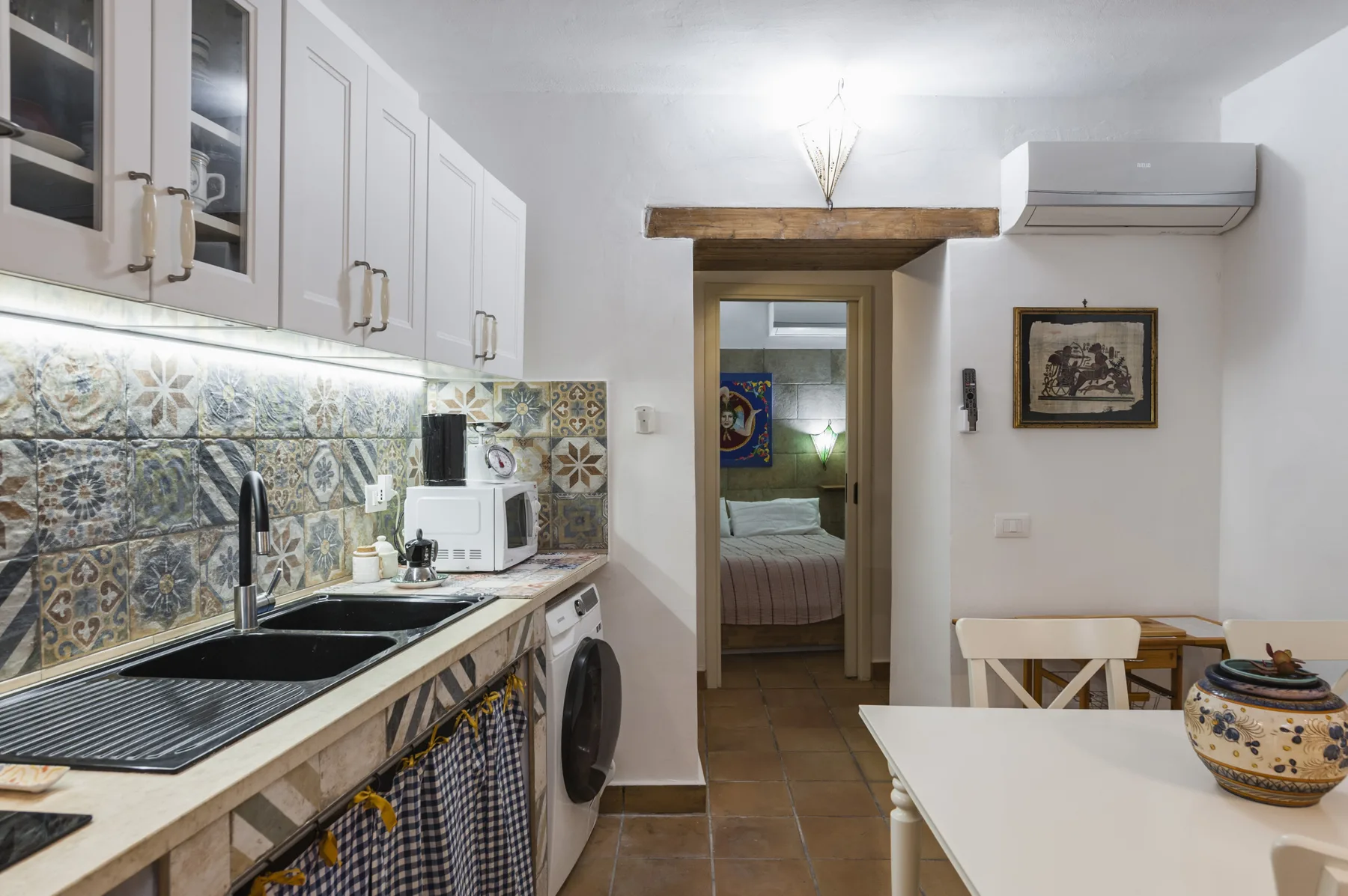 Una cocina compacta con salpicadero de azulejos estampados y una puerta hacia un dormitorio.