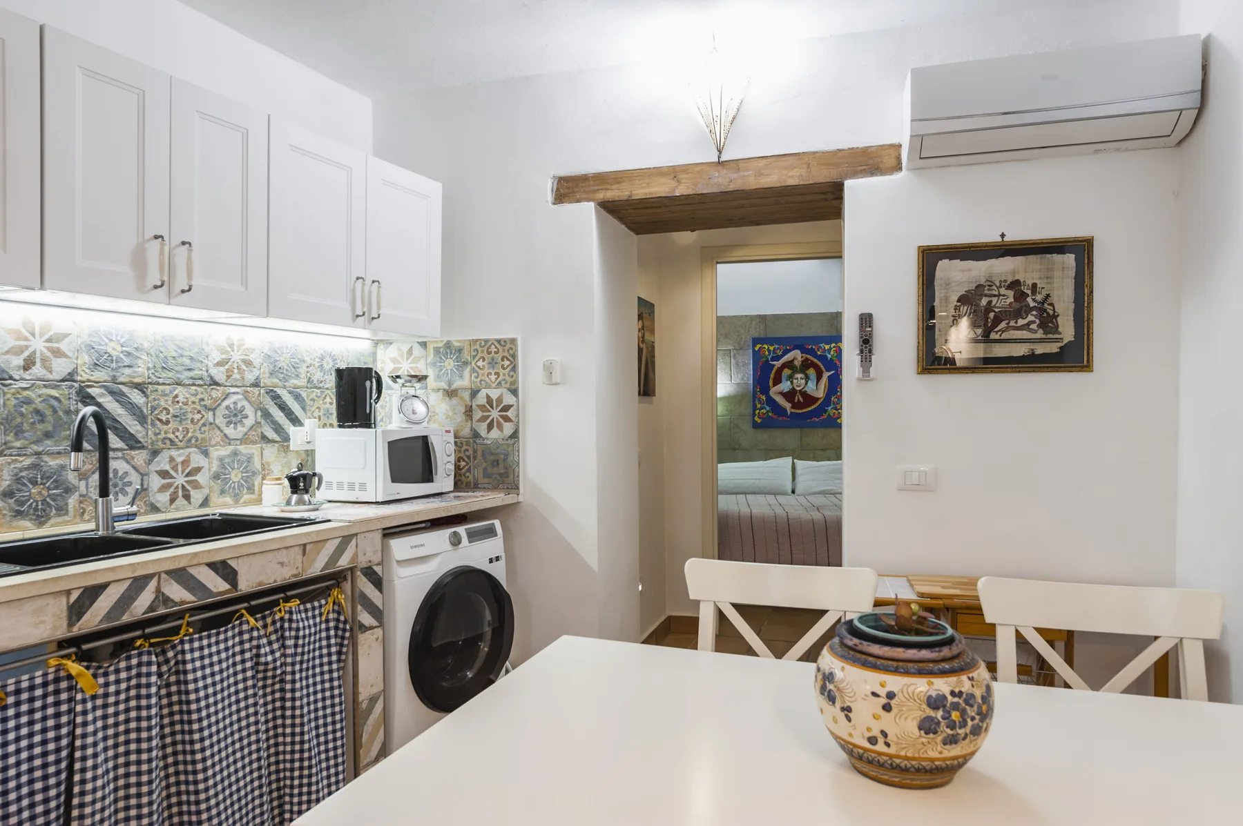 Una cocina compacta y zona de comedor con azulejos decorados y una mesa.