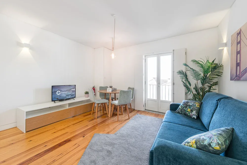 A bright living room with a blue sofa, dining table, and balcony doors.