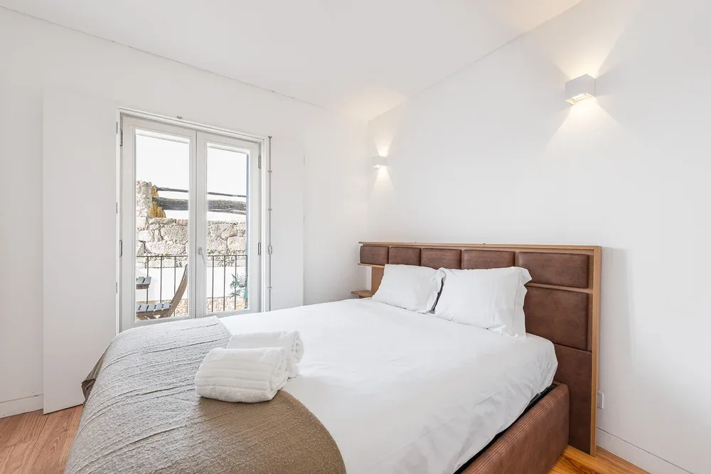 A bright bedroom with a bed beside tall glass doors.