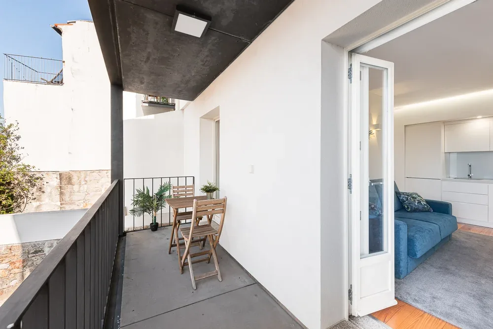 A narrow balcony with a small table and chairs beside an open door.