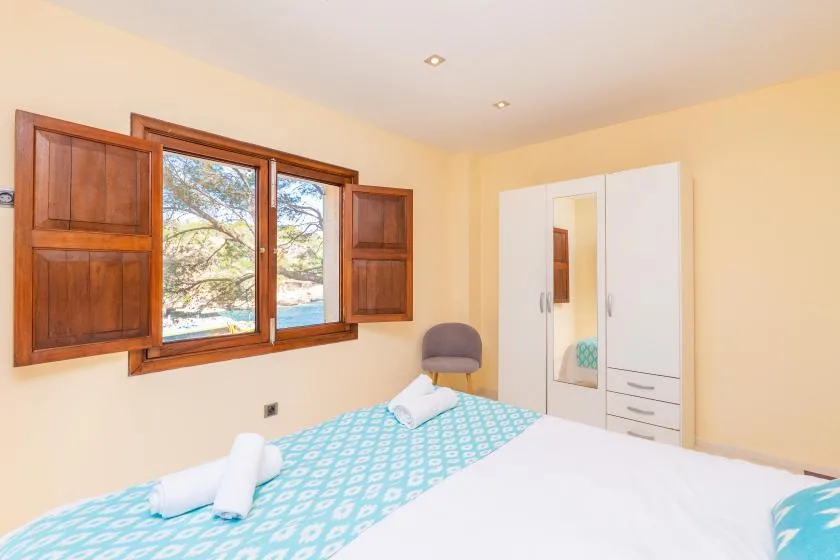 A bedroom with a bed, a wooden-framed window, and a wardrobe.