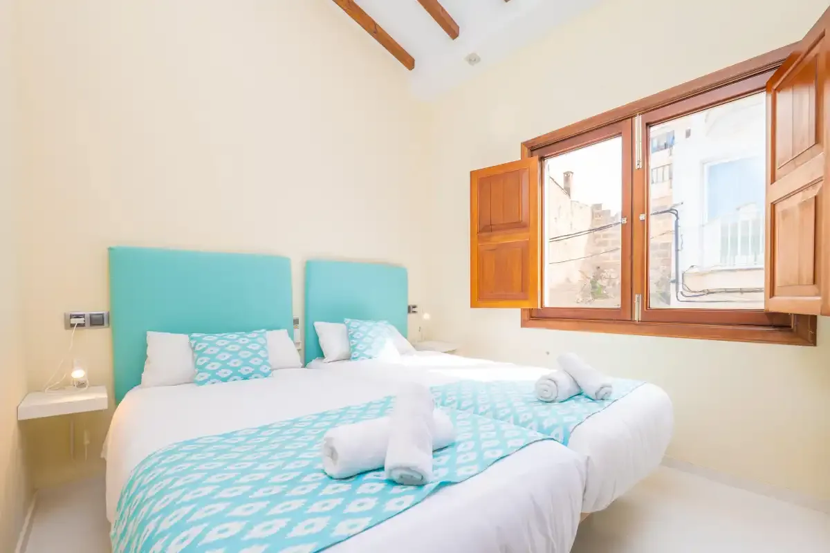 A bright bedroom with two beds dressed in white and turquoise linens.