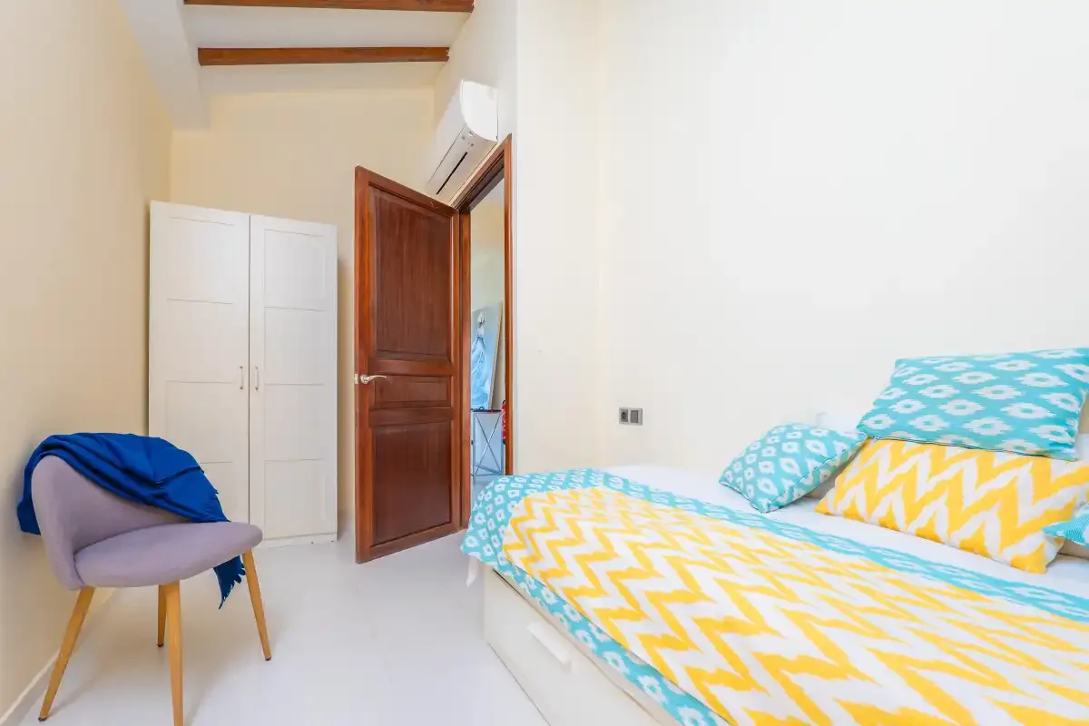 A bedroom with a colorful bed, a chair, and an open wooden door.