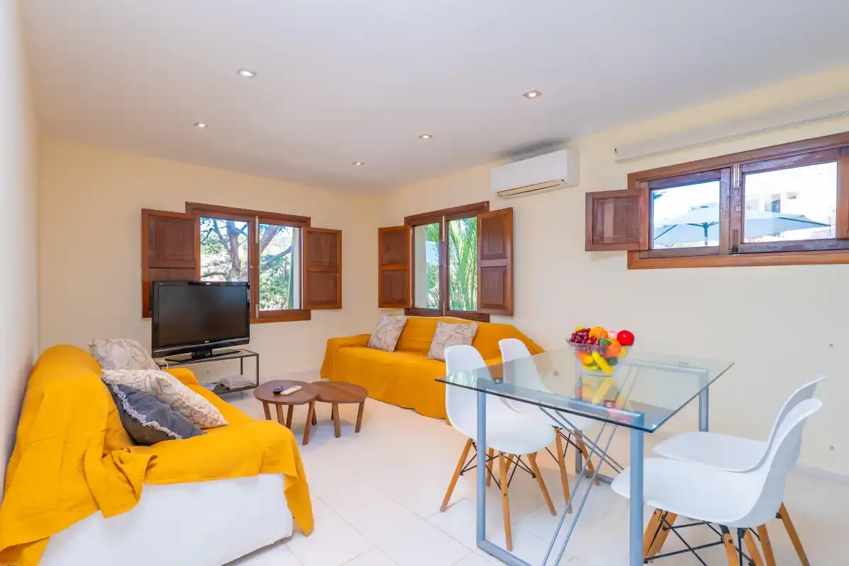 A bright living and dining area with yellow seating and a glass dining table.