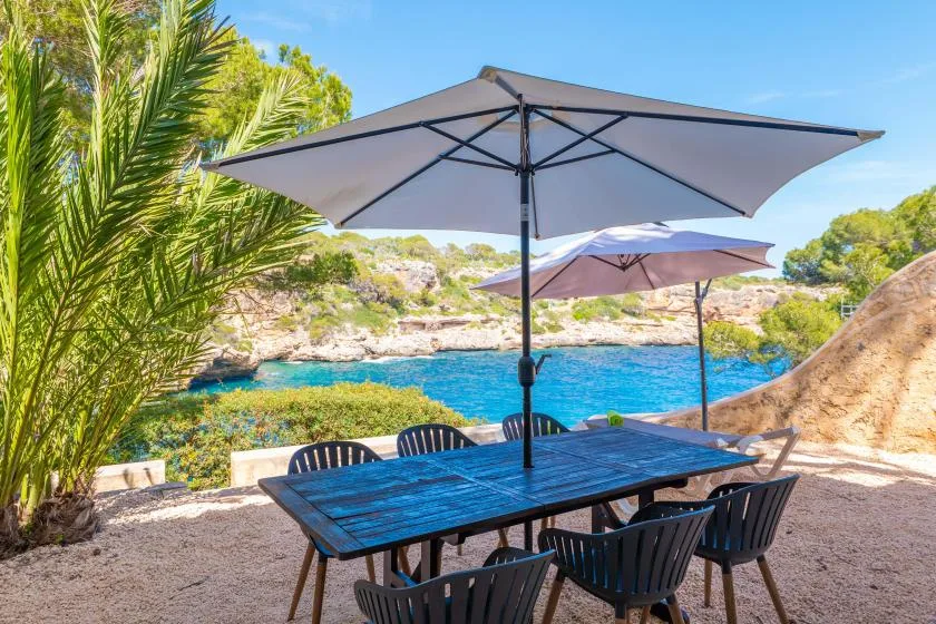 An outdoor dining area with a table and umbrellas beside a blue sea.