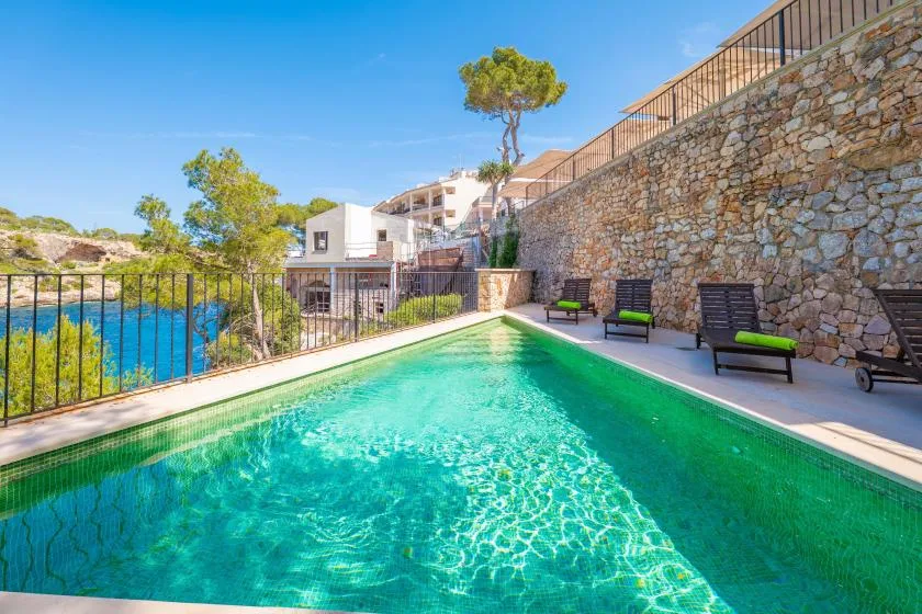 A swimming pool beside a stone wall and outdoor seating.