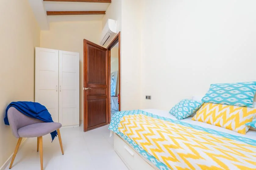 A bedroom with a bed covered in colorful patterned bedding and a chair.