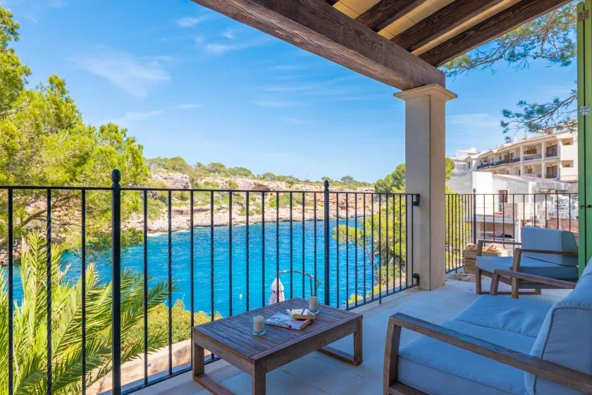 A covered patio with seating overlooks bright blue water and a tree-lined shore.
