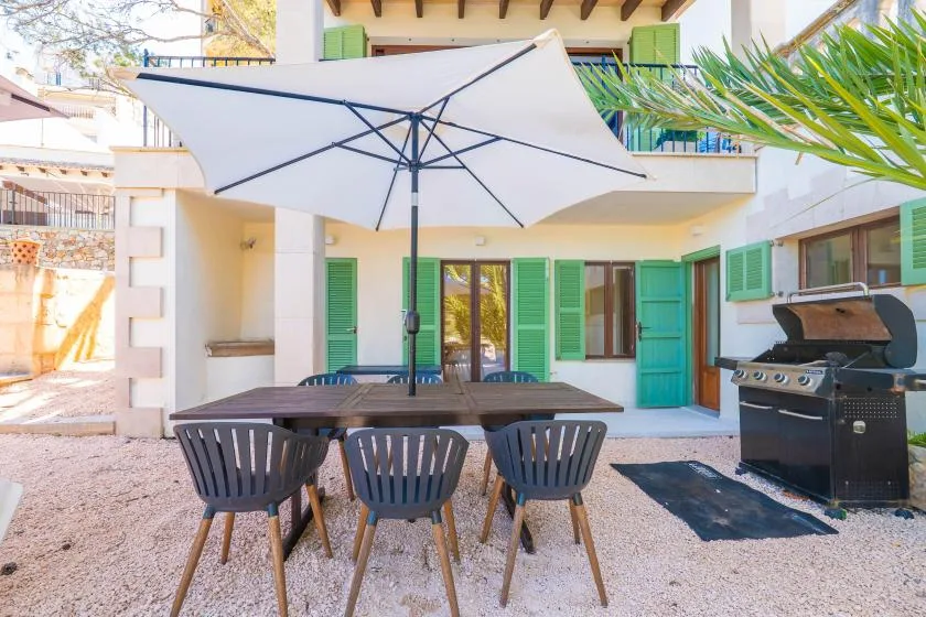 An outdoor patio with a dining table beneath a large umbrella and a grill nearby.