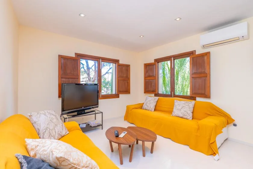 A living room with yellow seating, a television, and windows with wooden shutters.