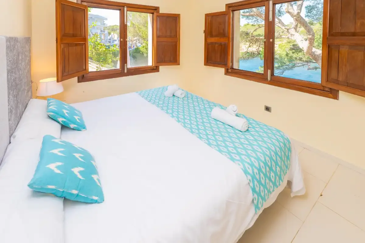 A bedroom with a neatly made bed and open wooden shutters.