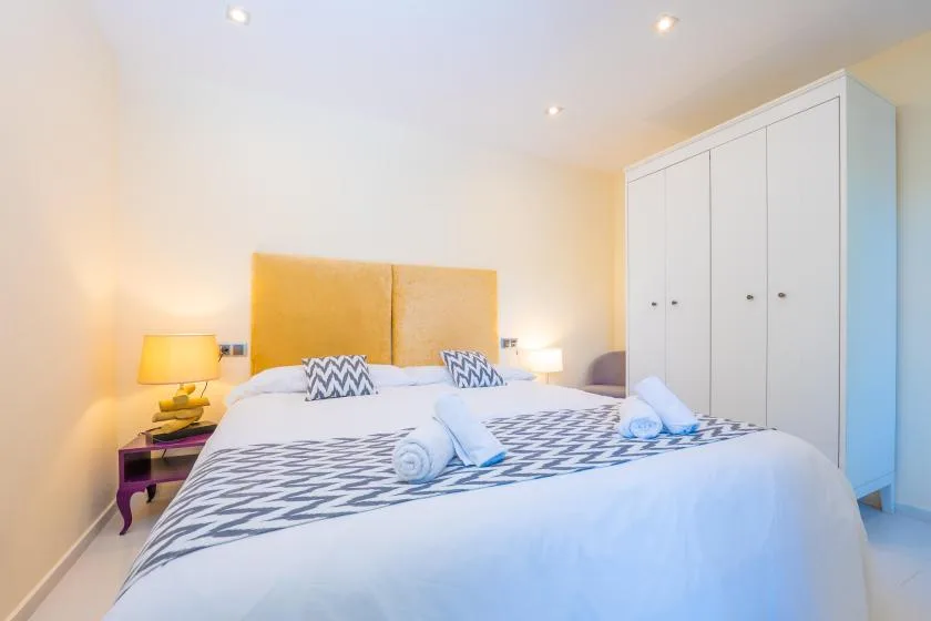 A bright bedroom with a neatly made bed and a tall white wardrobe.