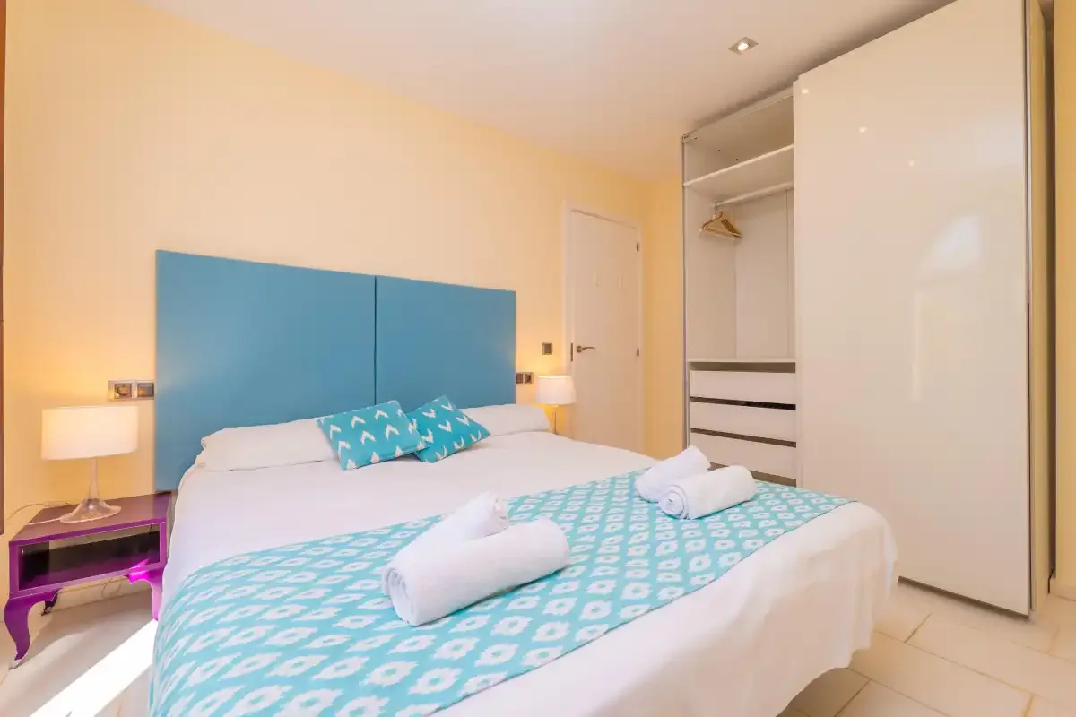 A bedroom with a bed, turquoise headboard, and folded towels.