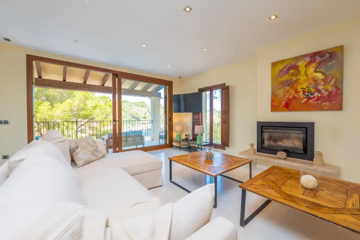 A bright living room with seating, two wooden coffee tables, and glass doors opening to a balcony.