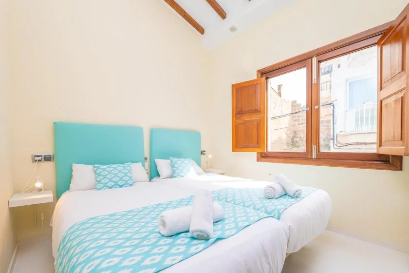 A bright bedroom with two beds, turquoise bedding, and a large window.