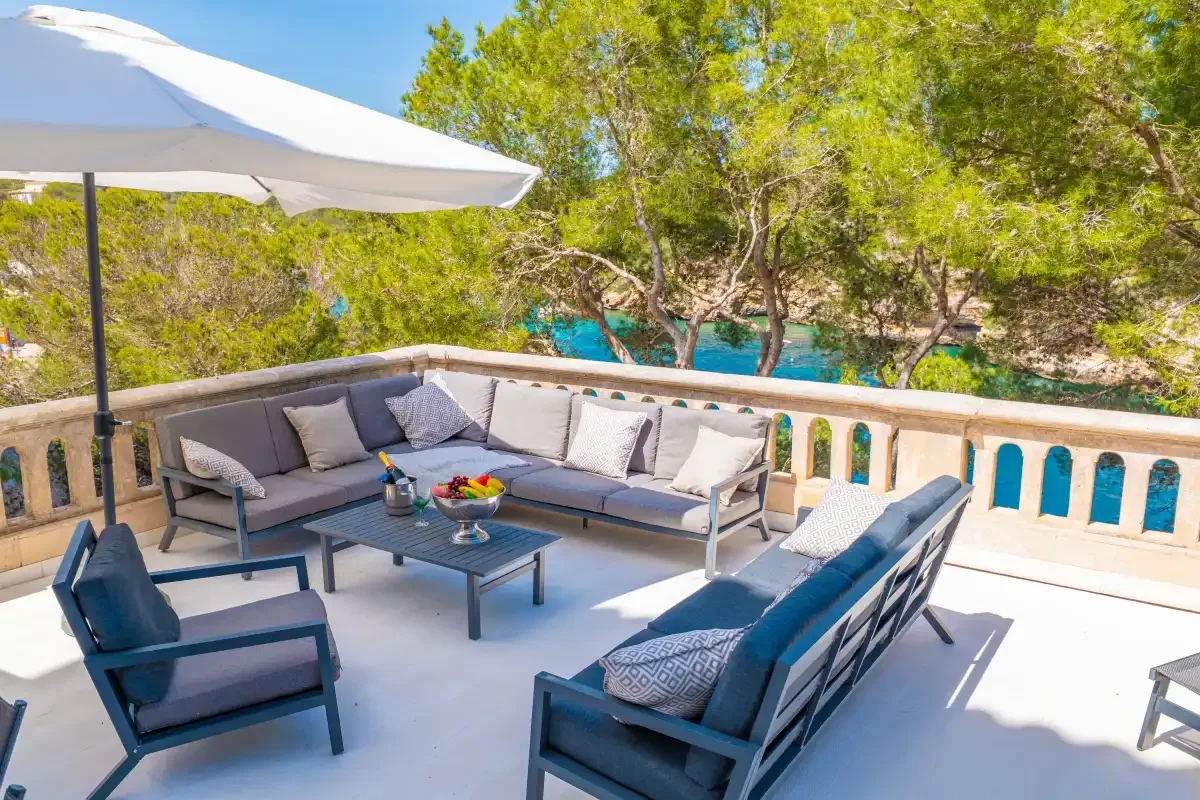 An outdoor seating area with cushioned furniture and a large umbrella overlooks trees.