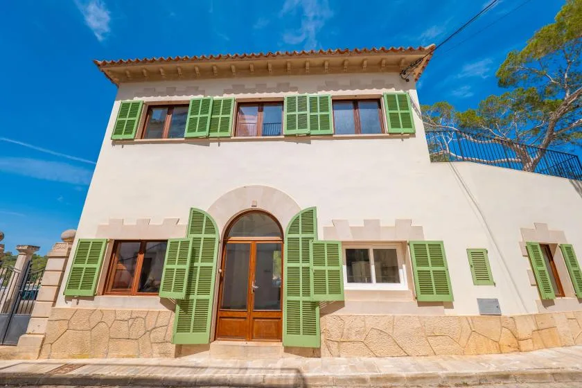 A white two-story building with green shutters and a central arched entrance.