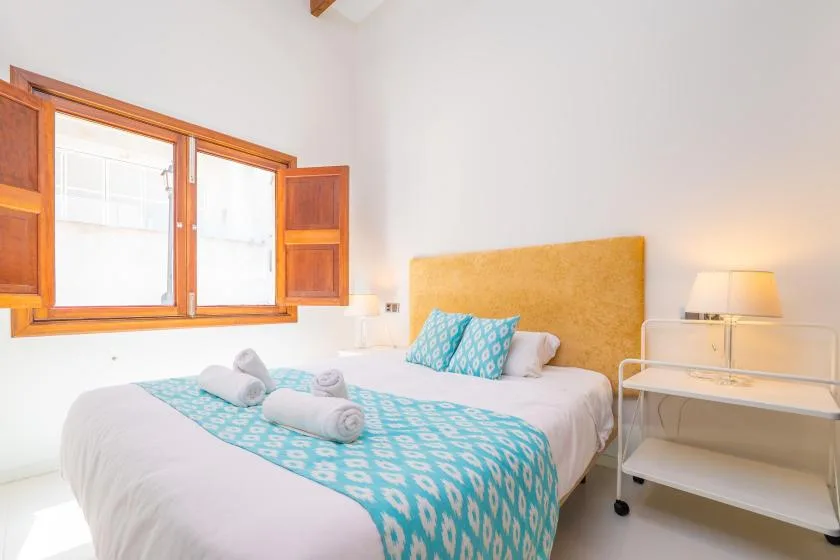 A bright bedroom with a bed dressed in white and turquoise bedding.