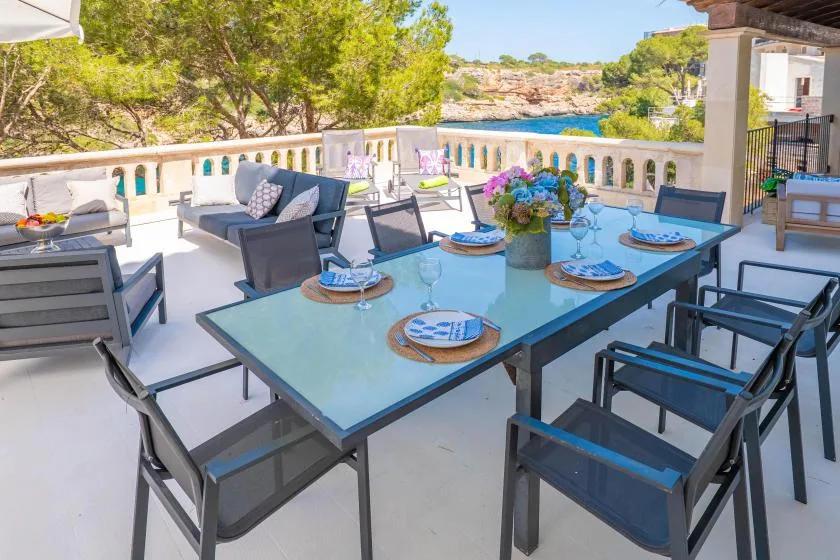 An outdoor dining terrace with a set table and seating overlooking the water.