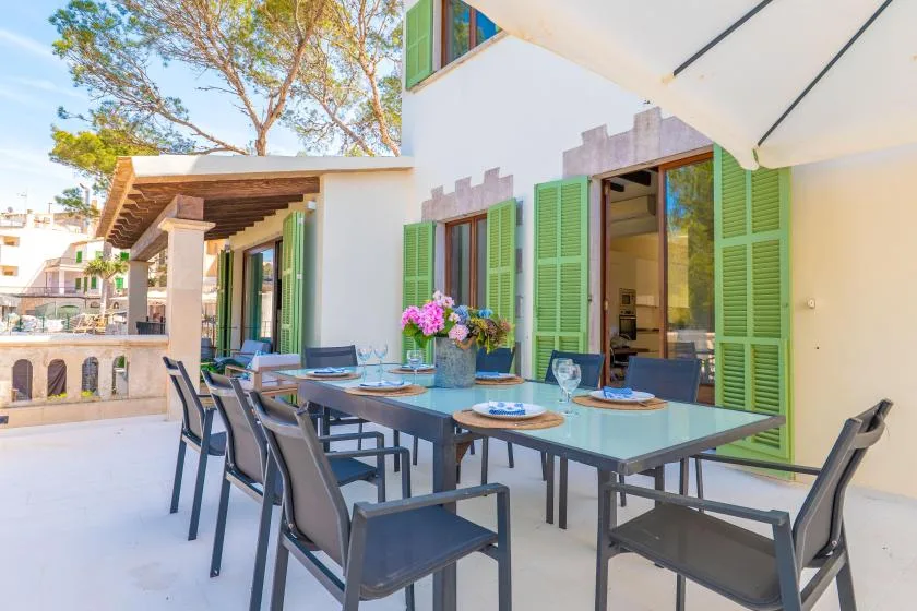 An outdoor dining area with a long table and green shutters.