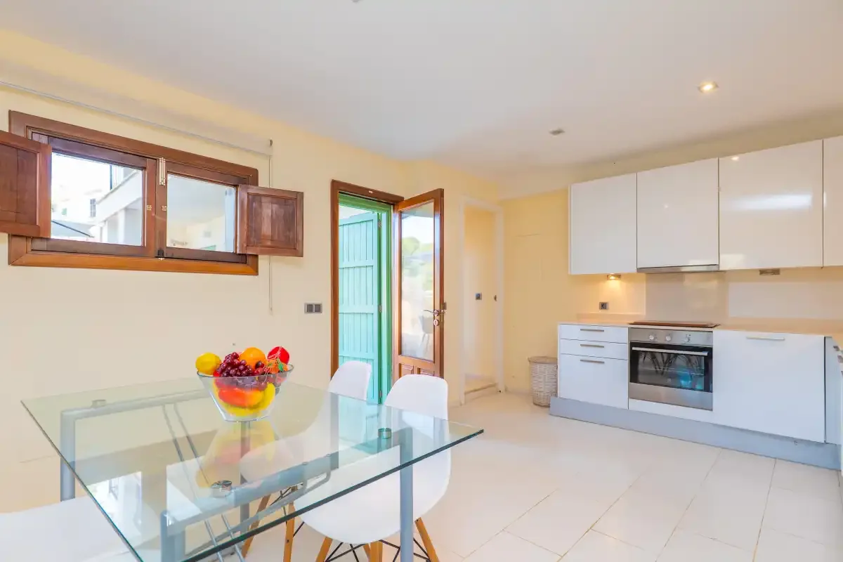 A bright kitchen and dining area with a glass table and white cabinetry.