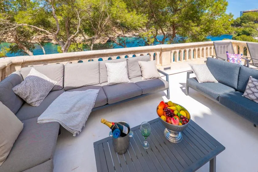 An outdoor terrace has cushioned seating and a coffee table beside the water.