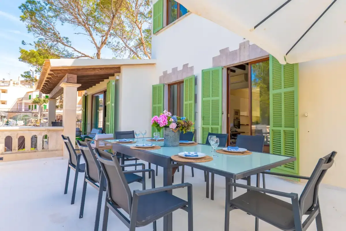 An outdoor dining area beside a white building, with green shutters and a table set for a meal.