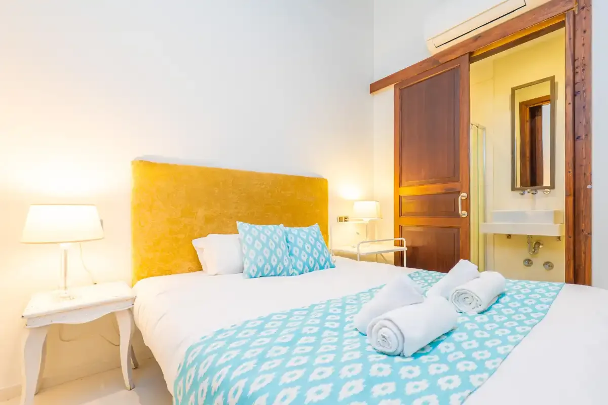A bedroom with a bed dressed in white and turquoise linens.