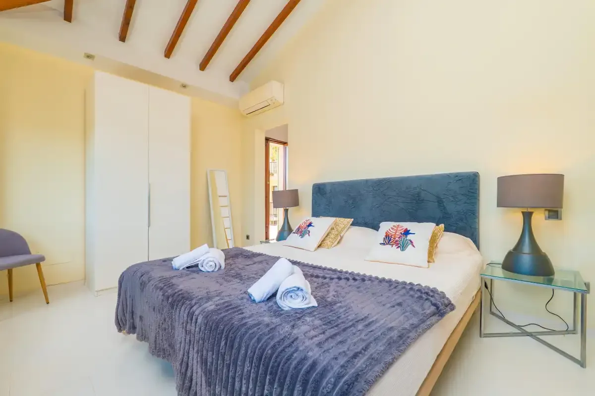 A bedroom with a bed, bedside lamps, and exposed wooden ceiling beams.