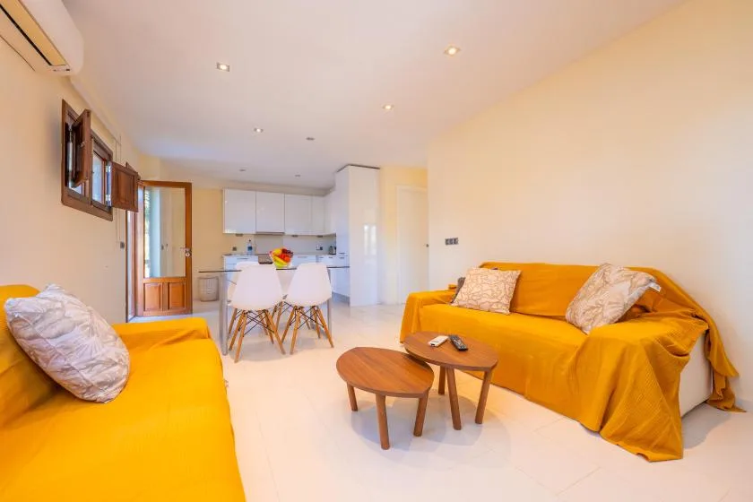 A bright living room with orange seating and a small dining area beside the kitchen.