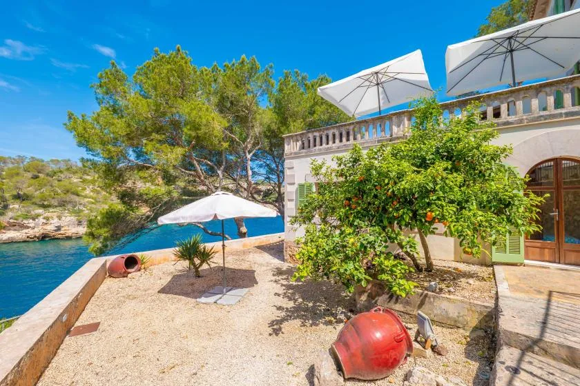 A seaside terrace with white umbrellas overlooks clear blue water.