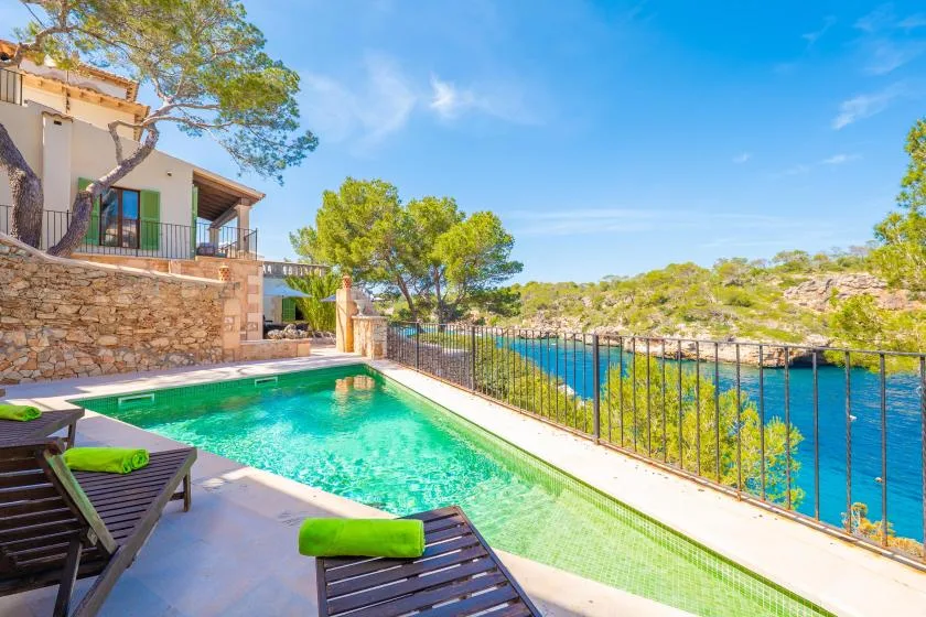 Una piscina junto a una casa costera tiene vistas al agua azul y una costa arbolada.