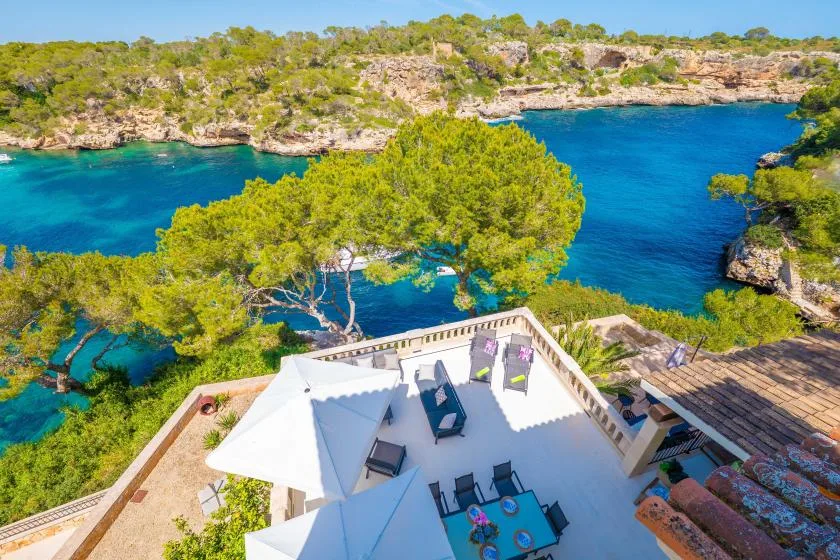 A terrace overlooks a vivid blue coastal inlet surrounded by greenery.