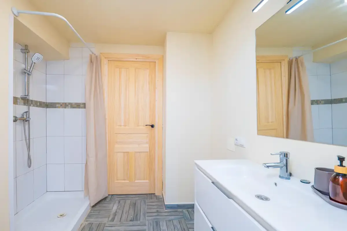 A bathroom with a shower, wooden door, and white sink counter.