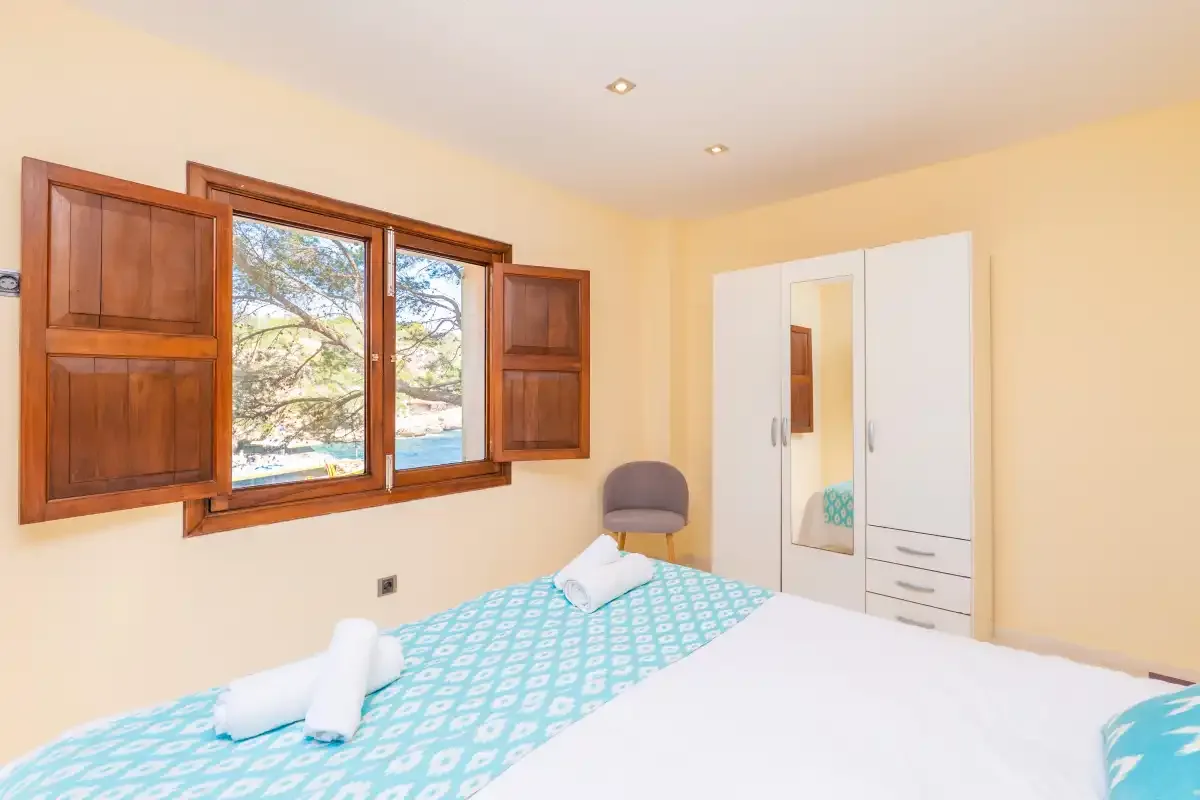 A bedroom with a bed, wooden window shutters, and a white wardrobe.