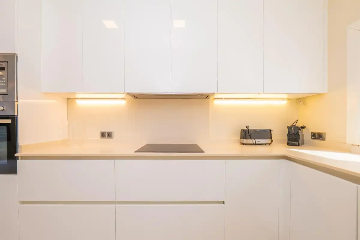 A modern kitchen with white cabinets, a cooktop, and countertop appliances.