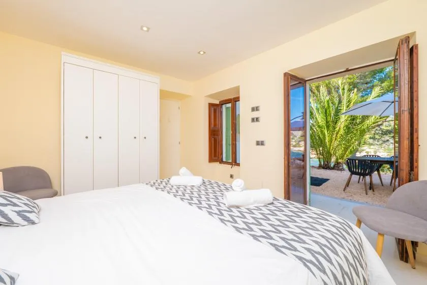 A bedroom with two beds and an open doorway overlooking a leafy outdoor patio.